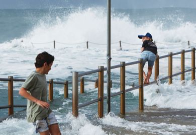 Two boys are seen avoiding large waves washing through the closed ocean pool at Dee Why Point, Sydney, Australia 