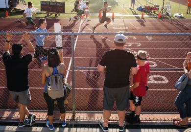 People watch from behind the fence as the athletes cross the finish lin People watch from behind the fence as the athletes cross the finish line as a metaphor for the wealth gap widening as US elite report record enrolments