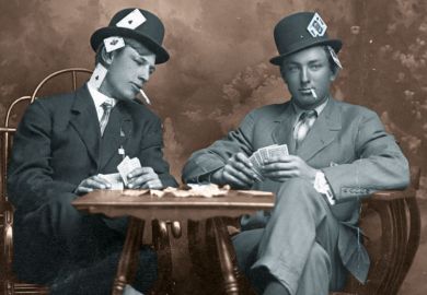 Two young men pretending to play cards. They are smoking and they sit close to a small table. Both men wear hats and have their legs crossed. One man is peeking into the other's card hand. Both guys have aces, kings and other cards visibly hidden in all p