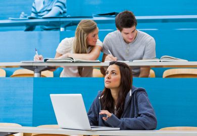 Students sitting in lecture with girl thinking at laptop Students sitting in lecture with girl thinking at laptop