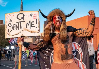 Jake Angeli, 33, aka Yellowstone Wolf, from Phoenix, holds a QAnon sign, as he presents himself as a shamanist and consultant for the Trump supporters gathered in front of the Maricopa County Election Department where ballots are counted after the US pres