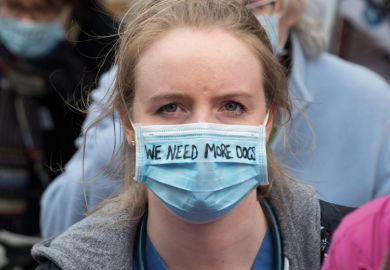A woman doctor wears a surgical mask with the writing 'We need More Docs'  A woman doctor wears a surgical mask with the writing 'We need More Docs' to illustrate More medical students ‘won’t solve doctor shortage alone’