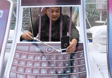Person with arms behind art installation bars holding his mobile phone other side of bars