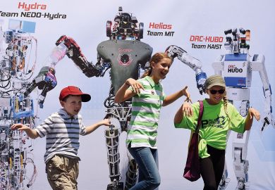 Children pose in front of a promotional poster during the finals of the DARPA Robotics Challenge to illustrate Canada joining the rush to create a Darpa