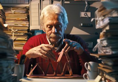 Unproductive senior office worker sitting at desk and building a card castle instead of working