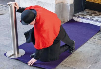 Person in bowler hat  flattens a doorway carpet before an event for special guests to illustrate 'finding a new v-c brings hug responsibility'