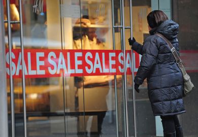 A woman enters a shop displaying a sale sign for Smaller US colleges try big fee cuts to tempt students back