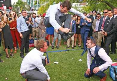 A man jumps over two men who have their ties tied together as they play a game of Limbo in Melbourne, Australia.    A man jumps over two men who have their ties tied together as they play a game of Limbo in Melbourne, Australia to illustrate Australian universities ‘already near’ overseas enrolment caps