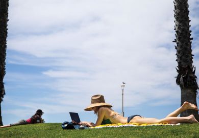 Person sunbathing in a bikini with her laptop 