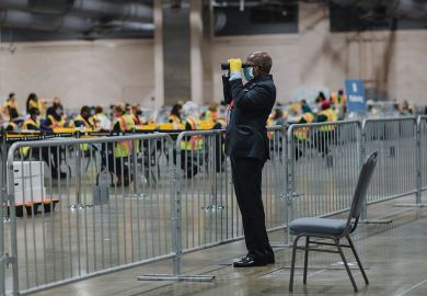 An official poll watcher uses binoculars as workers count ballots for the 2020 Presidential election.