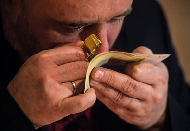 An employee examines with magnifier glass counterfeit 200 Euro bank note to illustrate Problems with bank checks drive student visa refusals