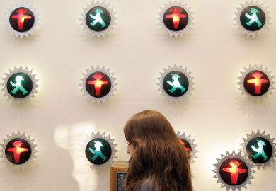 Person walking past a wall with a number of little traffic lights with a red and green man in the centre of each. Person walking past a wall with an number of little traffic lights of red and green man in the centre of each as a metaphor for confused communication