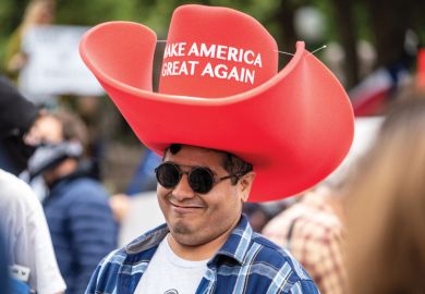 A person wears an oversized "Make America Great Again" hat as a metaphor for the US lawmakers to adopt philanthropic tactics for dictating academic content