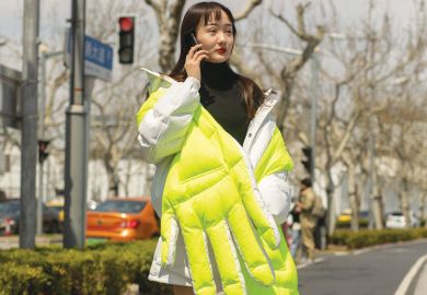 Lady wearing wearing neon quilted large hand design in Shanghai, China as a metaphor for a rigid system pushes Chinese students to use private agents.