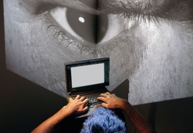  Man sits at laptop computer with image of giant eye on a big screen as a metaphor to show the online behaviour of Eric Chabriere.