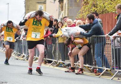 Competitors in a coal carrying race with large heavy sack on their back and one man from a crowd helping a sack on a competitors back as a metaphor  to Crowdfunding is increasingly a way for scholars and students at less prestigious universities to gain r