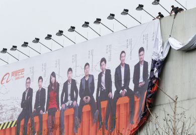 Two people setting up a large billboard of an image of a row of people sitting in a line at the Alibaba Group headquarters for Students seeing little benefit from Chinese start-up drive