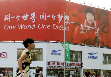 Person walking past a poster reading 'One World One Dream' in English and Chinese as a metaphor for Taiwan eyes international recruitment with switch to English.