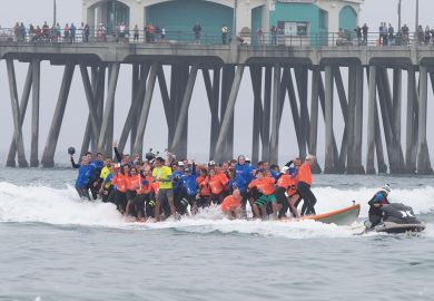 Crowds gather on the pier and the beach to watch surfing break the World Guinness Record for most people (66) on a surfboard and the biggest surf board (42 1/4 feet) in Huntington Beach, California to illustrate Biden officials open to more three-year deg