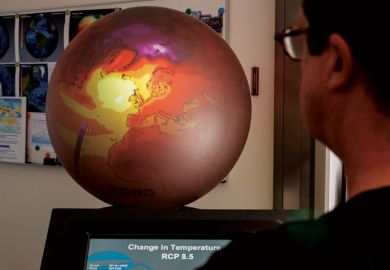 Person looking at screen next to supercomputer with red globe on top Person looking at screen next to supercomputer with red globe on top