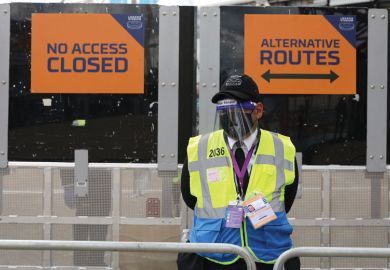 A steward in PPE including face mask and visor as a precaution against COVID-19 staffs a barrier at The London Stadium