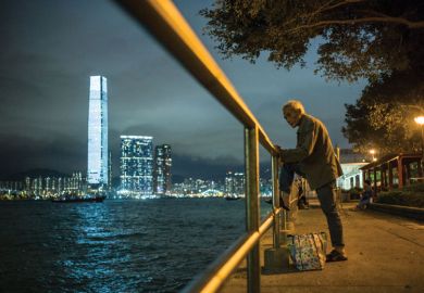 An elderly man rests his foot on a railing as he fishes in the waters of Victoria Harbour in Hong Kong