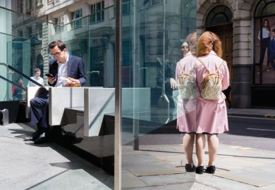 Businessman inside building looking at phone, woman standing outside as a metaphor for gender split: degrees aren’t paying off for women