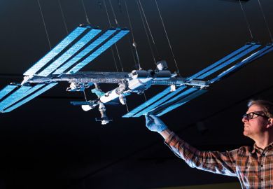 A technician with a Lego model of the International Space Station to illustrate 'Does business logic mean that we should break up universities?'