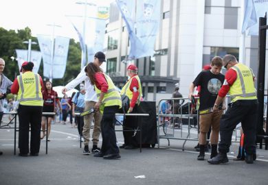 Crowd safety personnel inspecting bags of attendees outside a sports stadium Crowd safety personnel inspecting bags of attendees outside a sports stadium