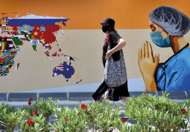 A woman wearing face mask walks past a mural depicting of a healthcare worker and a world map with flags on walls 