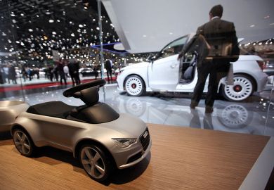 A toy car for Audi AG is seen on the company's stand with a man looking at white car in background