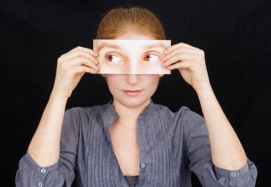 Woman holding print-out of eyes over face Woman holding print-out of eyes over face