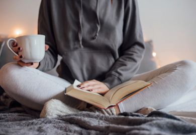 Woman reading book and drinking tea on bed