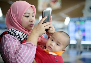 A woman with a baby looking at her phone at an airport. To illustrate that online marketing to prospective international students states that they would be eligible to bring family members with them, despite the UK government’s dependants visa ban.