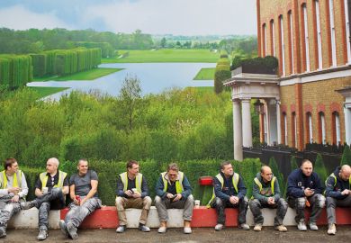 Workmen sit in front of hoarding depicting English country house and grounds