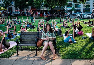 Woman on bench with outdoor yoga class behind her Woman on bench with outdoor yoga class behind her, illustrating lifelong learning