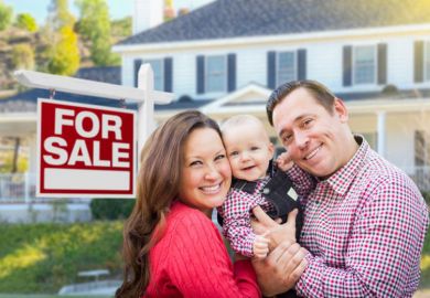 Young couple with baby next to house for sale sign Young couple with baby next to house for sale sign