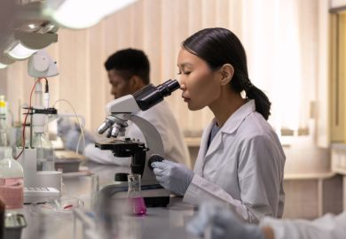 Young female scientist looking in microscope