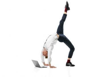 young flexible man doing backbend and typing on laptop