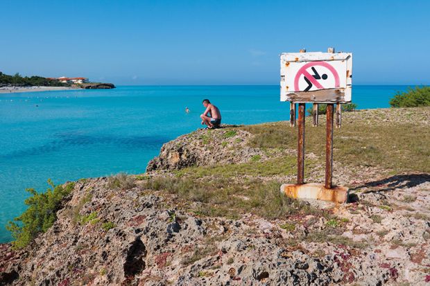 Man looking at the ocean next to a No Swimming sign Man looking at the ocean next to a No Swimming sign