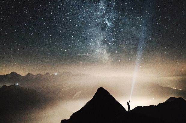 A man shining a torch up to the stars