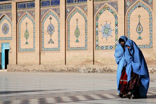 Two women in blue burqas walk at the front of a mosque with a door open, symbolising an open university