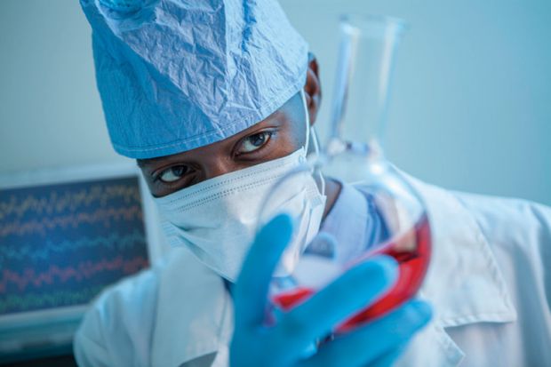 An academic studying red liquid in a glass flask An academic studying red liquid in a glass flask