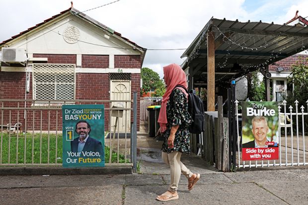 A woman walks past campaign signs depicting candidates in Lakemba, Australia, 12 March 2025. 