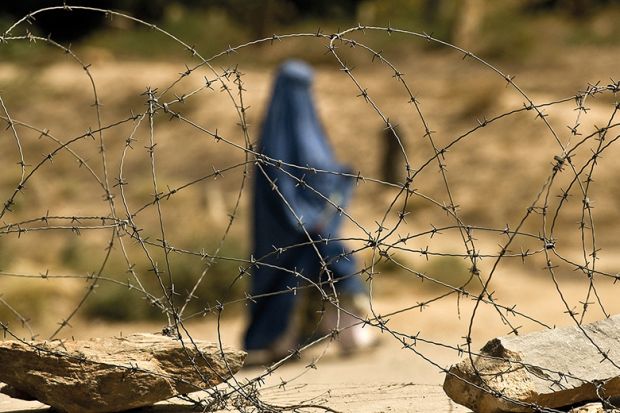 A covered Muslim woman walks behind some barbed wire A covered Muslim woman walks behind some barbed wire