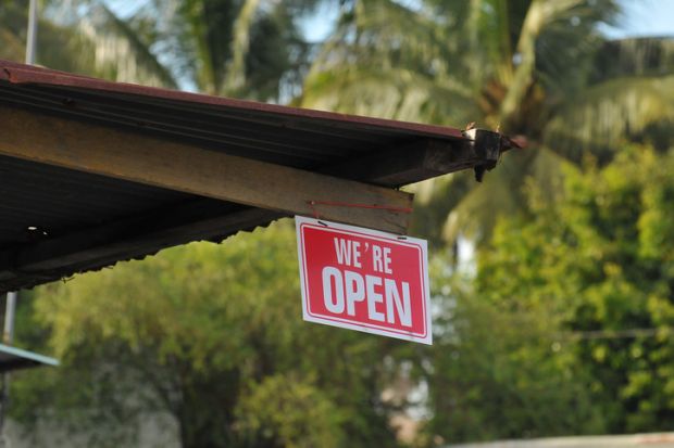 A building with plam trees behind it and a 'we're open' sign, illustrating branch campuses 