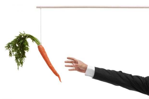 Businessperson's hand reaching for carrot on stick Businessperson's hand reaching for carrot on stick