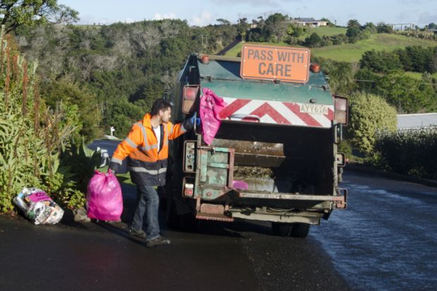 Cable Bay, New Zealand - July 25, 2013 Waste management worker throws rubbish into a rubbish truck on the side of the road Cable Bay, New Zealand - July 25, 2013 Waste management worker throws rubbish into a rubbish truck on the side of the road
