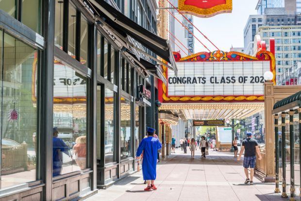 Chicago, IL  USA - May 24,2020 A young man in cap and gown walks under a sign downtown at the Chicago Theater, saying Congrats Class of 2020.