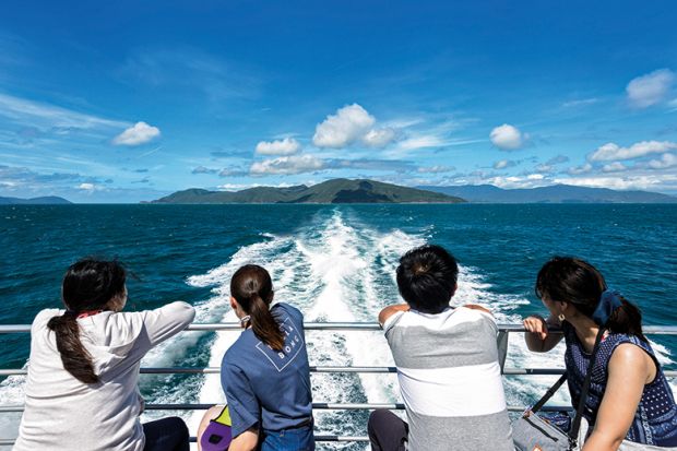 Chinese tourists looking back at the boat wake while cruising at the Great Barrier Reef, Far North Queensland, Australia. To illustrate declining research collaboration between China and Australia Chinese tourists looking back at the boat wake while cruising at the Great Barrier Reef, Far North Queensland, Australia. To illustrate declining research collaboration between China and Australia